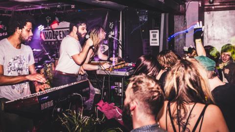 Rock band Flamingrods - including the singer, keyboard player and guitarist - on stage at The Boileroom in front of a crowd of people dancing