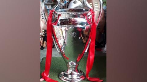 Picture shows a replica Champions League Trophy with red ribbon tied to it.