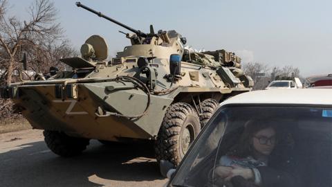 A refugee waits in a car as an armoured personnel carrier of pro-Russian troops drives out of a checkpoint in the course of Ukraine-Russia conflict in the besieged southern port city of Mariupol, Ukraine, 24 March 2022.