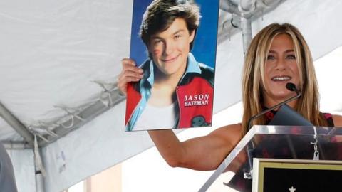 Jennifer Aniston holding Jason Bateman poster