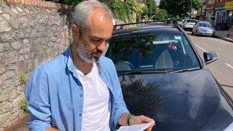 A man stood in front of his car holding a leaflet