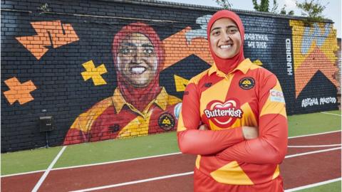 Abtaha Maqsood standing next to her mural