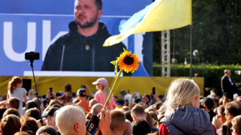 The public looks on while Ukrainian President Volodymyr Zelensky addresses the crowd at Lukiskiu Square in Vilnius on 11 July 2023, during a NATO Summit