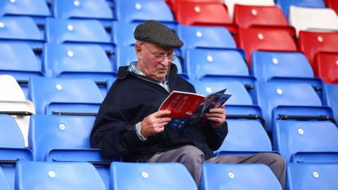 A man reads the matchday programme at Selhurst Park