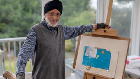 Sardul Gill, inside his house, stood beside one of his pictures, which consists of a rectangle of blue paper with a rectangle of foil on top