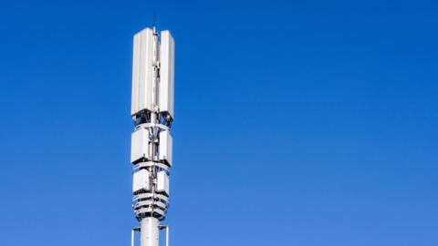 A tall post in the city with 5G mobile phone telecoms signal equipment against a clear blue sky.