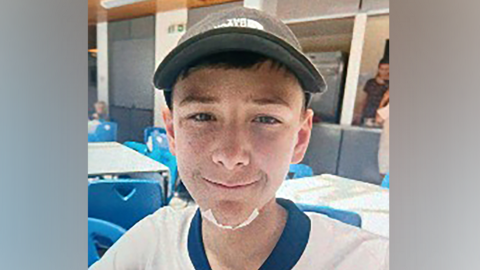 Mylo smiling into the camera. He is wearing a grey cap and England football shirt. He has a plaster on his chin.