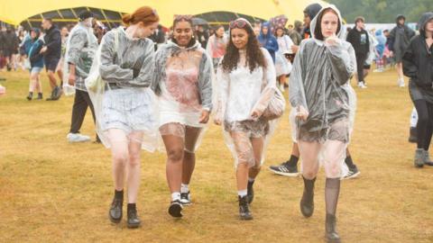 Four women wearing raincoats walk through festival site