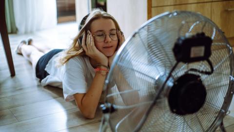 A girl lies on the floor in front of a fan.