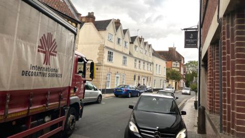 A lorry enters a street with cars parked on either side in the Colegate area of Norwich. 