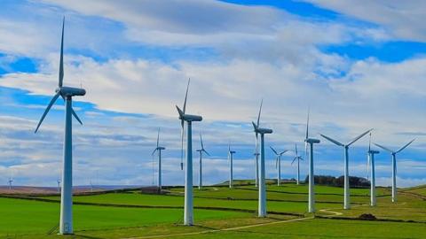 A row of wind turbines in rural fields under a sky of broken cloud