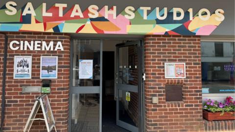 Red brick building with open door and bright and colourful "Saltash Studios" banner and the words Cinema on the side. 