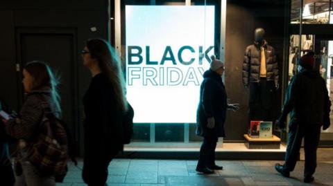 Shoppers walk past a Black Friday sign in a store window