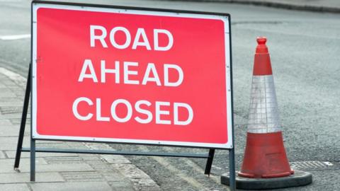 A road closed sign on a road a next to a bollard