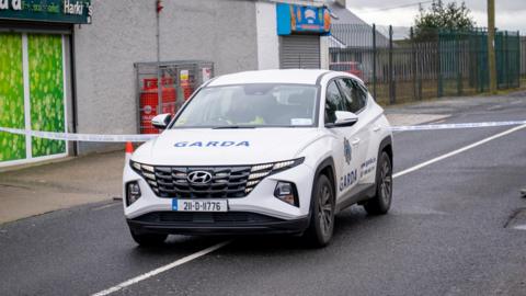 A garda car is parked on an empty road. Police tape is up.