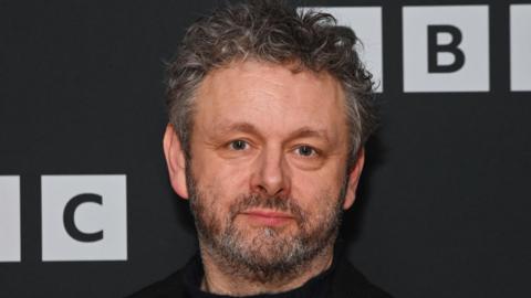 A picture of Michael Sheen at a photo call for BBC drama "The Way" at the BFI Southbank on February 5, 2024 in London, England. It is a close up image of Sheen's face. He is standing in front of the BBC background. 