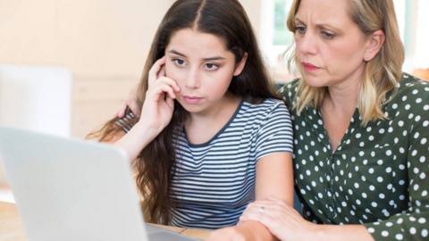 Girl and adult female sat together looking at laptop screen