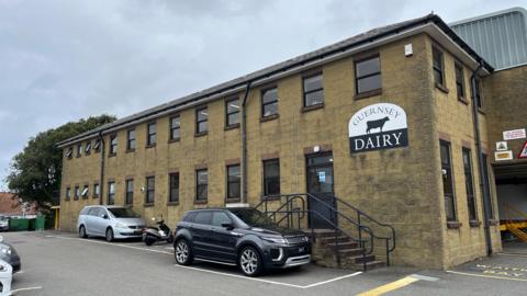 Guernsey Dairy - A building with yellow walls and a sign that says Guernsey Dairy, with the black outline of a Guernsey cow on it. 