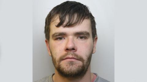 A police photo of Shane Phillips. He is white, with a brown beard and brown hair.