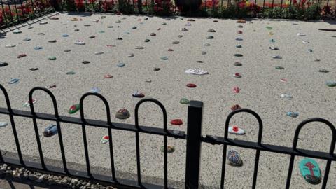 Brightly coloured pebbles are placed in resin in the ground surrounded by a short metal fence.