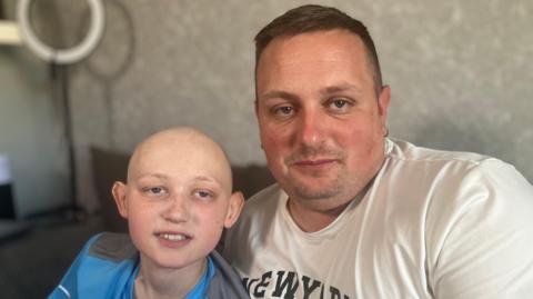 Harrison is pictured with his dad Mitchell on the sofa at home in Leicester. Mitchell has lost his hair because of of his cancer treatment 