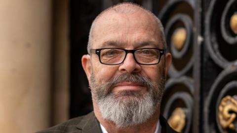 Royds councillor Stephen Place, who has short, shaved hair and a grey beard. He is wearing black-rimmed glasses.