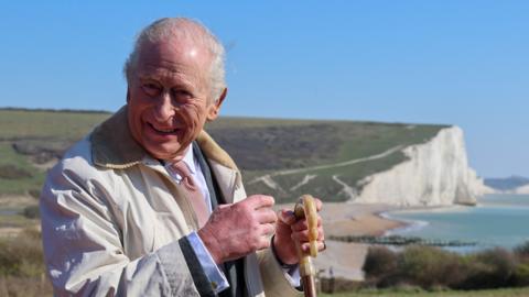 King Charles III stands in front of cliffs as he walks the King Charles III England Coast Path at Seven Sisters National Nature Reserve.
