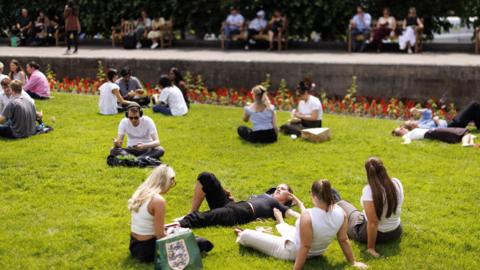 People picnic and enjoy the warm sunshine at St. Paul's Churchyard during lunchtime in the City of London financial district of London.