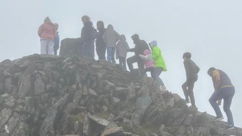 A line of people waiting to reach the trig point at the peak of Yr Wyddfa on a misty day