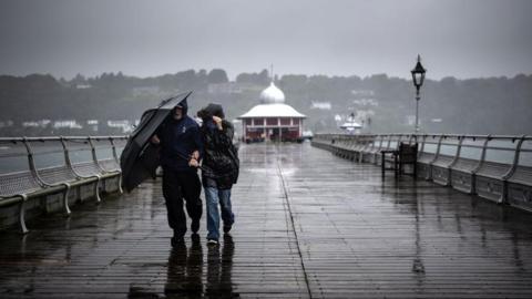 People walking along a pier with an umbrella on a wet and windy, grey day