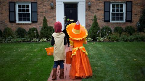 Two children dressed in costumes wait for sweets whilst trick or treating during Halloween.