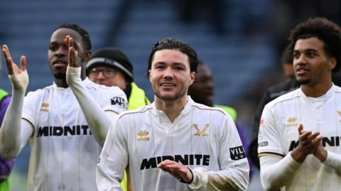 Sheffield United's Callum O'Hare smiling as he applauds fans in their white away shirt