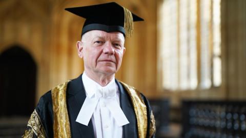 A headshot of Lord William Hague during his inauguration as the Chancellor of Oxford University at Sheldonian Theatre in Oxford. He is wearing a black and gold gown and cap with gold tassel. He is looking at the camera.