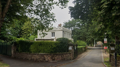 The school gates, flanked by a hedge. A white building stands to the right, along with a sign that reads "King Edward Camp Hill Schools"
