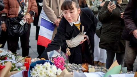 A woman lays flowers at a temporary memorial to the victims of the 13th November 2015 Paris terrorist attacks at Place de la Republique, on the tenth anniversary of the attacks, on November 13, 2025 in Paris, France.