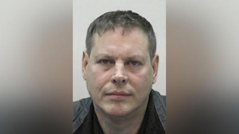 Mugshot of Steven Gauci. He is clean shaven with short dark hair tinged with grey and wearing a black and grey jacket.