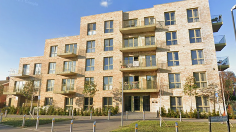 A part-five storey building containing 51 flats. They are made out of a sandstone-coloured brick and the picture was taken on a pleasant sunny day.