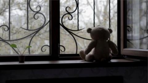 Stock image of a teddy bear in front of a window