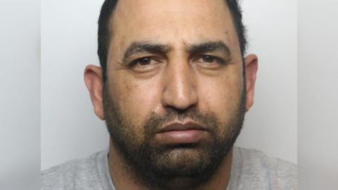 A police photo of Ifzal Hussain, a man wearing a grey t-shirt. 