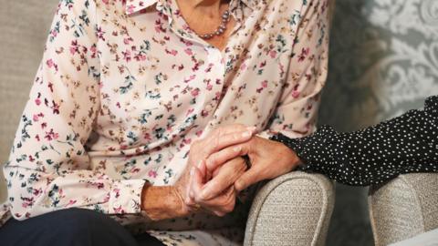 Two people seen from waist to neck holding hands while sitting down