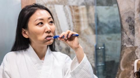 Woman facing a mirror and brushing her teeth