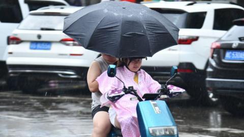 Two people ride a motorbike in Qionghai, Hainan Province of China amid driving rain.