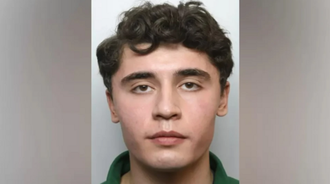 Daniel Khalife in his mug shot - he is looking straight at the camera, has short curly hair, and brown eyes with a neutral expression. A small part of his green polo shirt is visible.
