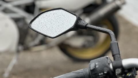 The wingmirror of a bike parked at the grandstand with raindrops on it.