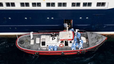 People being evacuated from cruise ship wearing protective clothing