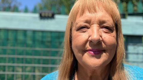 Linda, a woman with shoulder-length golden hair, wearing a blue top, smiling for the camera.