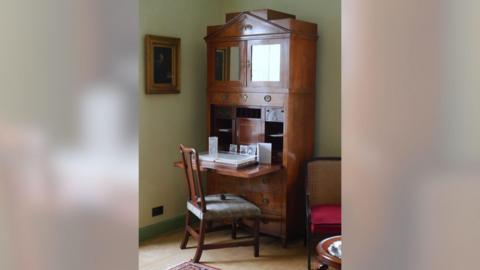 An old wooden writing desk in a green room.
