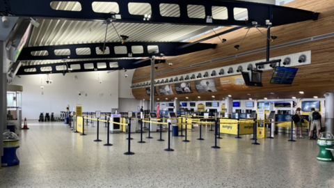 Interior of airport. Aurigny strap barriers lead passengers to front desks to check in. The airport is quiet with only a few people.