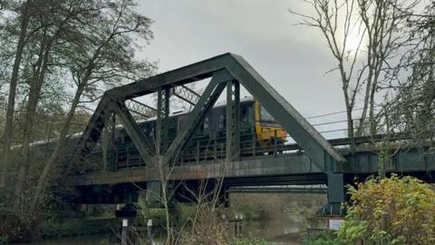 A green GWR train travels over the Shalford bridge over the River Wey