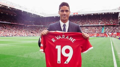 Raphael Varane poses on the pitch with his Manchester United shirt, with is number 19